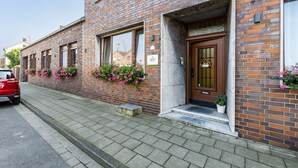 Ein Backsteinhaus mit Holztür, Fenstern und Blumenkästen am Gehweg.