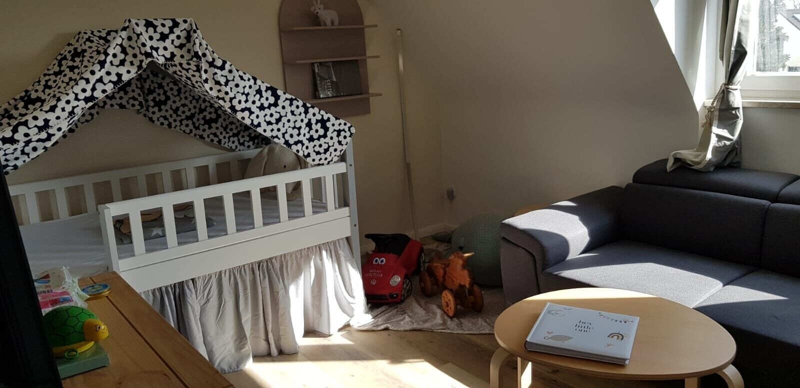 A cozy room with a white crib, a gray sofa, a small table, and a window with curtains.