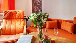 Een kamer met een leren fauteuil, een bank, een tafel met een boek, een vaas met bloemen en een fles.