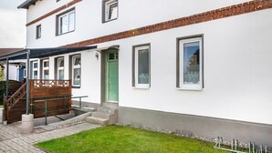 Een gebouw met twee verdiepingen, een witte gevel, een groene deur en een bakstenen detail.