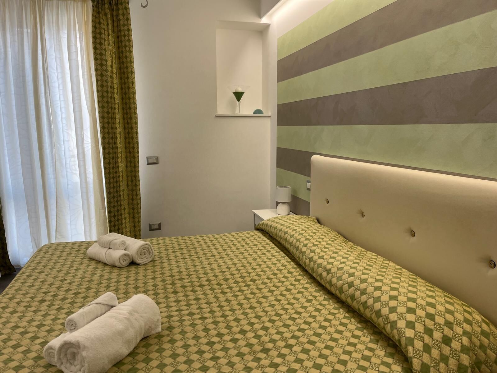 A hotel room with a bed, a nightstand, a lamp, and a wall with horizontal stripes.