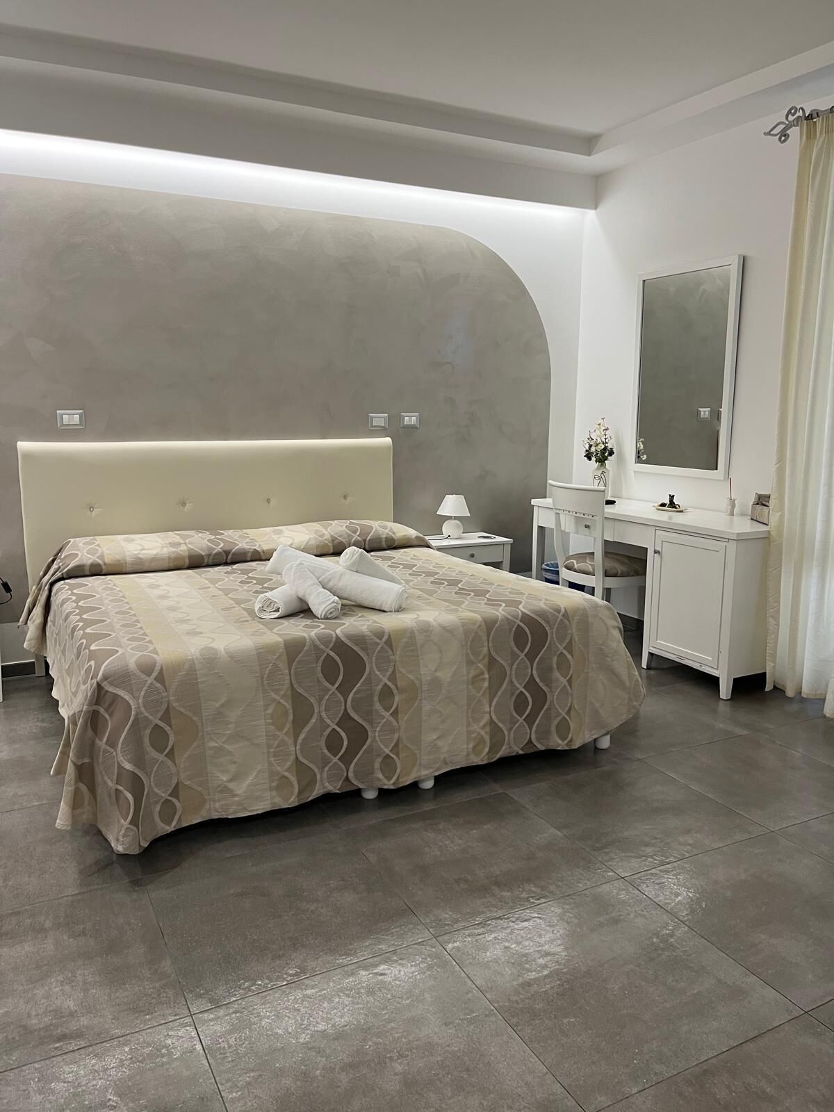A modern bedroom with two beds, a desk, and a large mirror.
