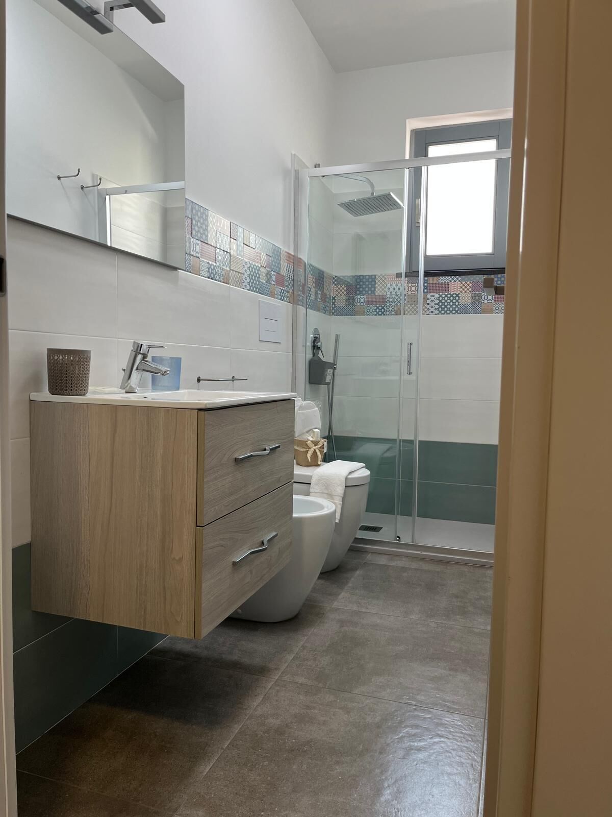 Een moderne badkamer met een houten wastafelmeubel, een douchecabine van glas en een betegelde spatwand.