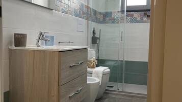 Een moderne badkamer met een houten wastafelmeubel, een douchecabine van glas en een betegelde spatwand.