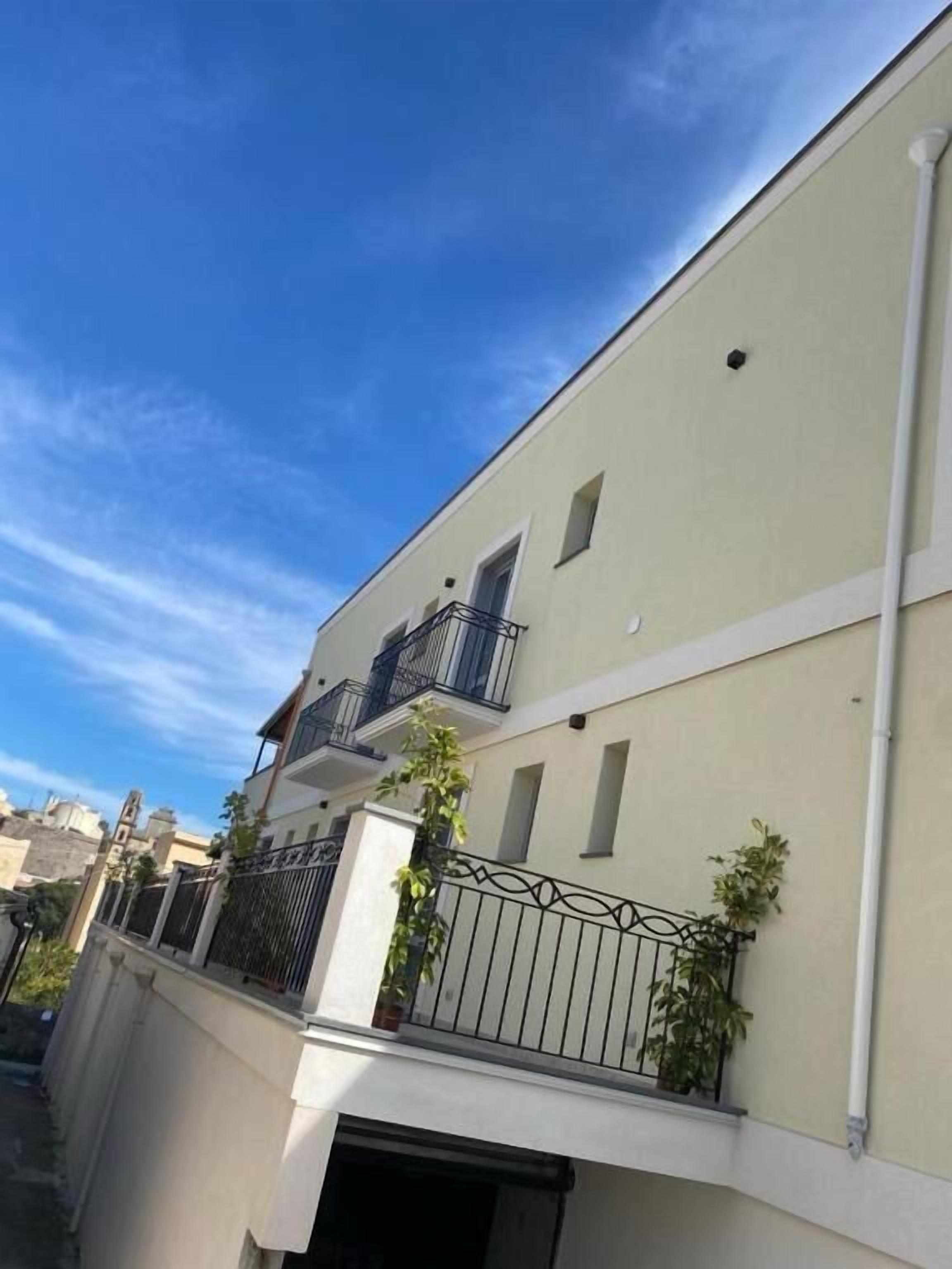 A multi-story building with balconies, a gated entrance, and a clear sky.
