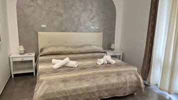 A neatly made bed with towels, a headboard, two bedside tables with lamps, and a large window with curtains.
