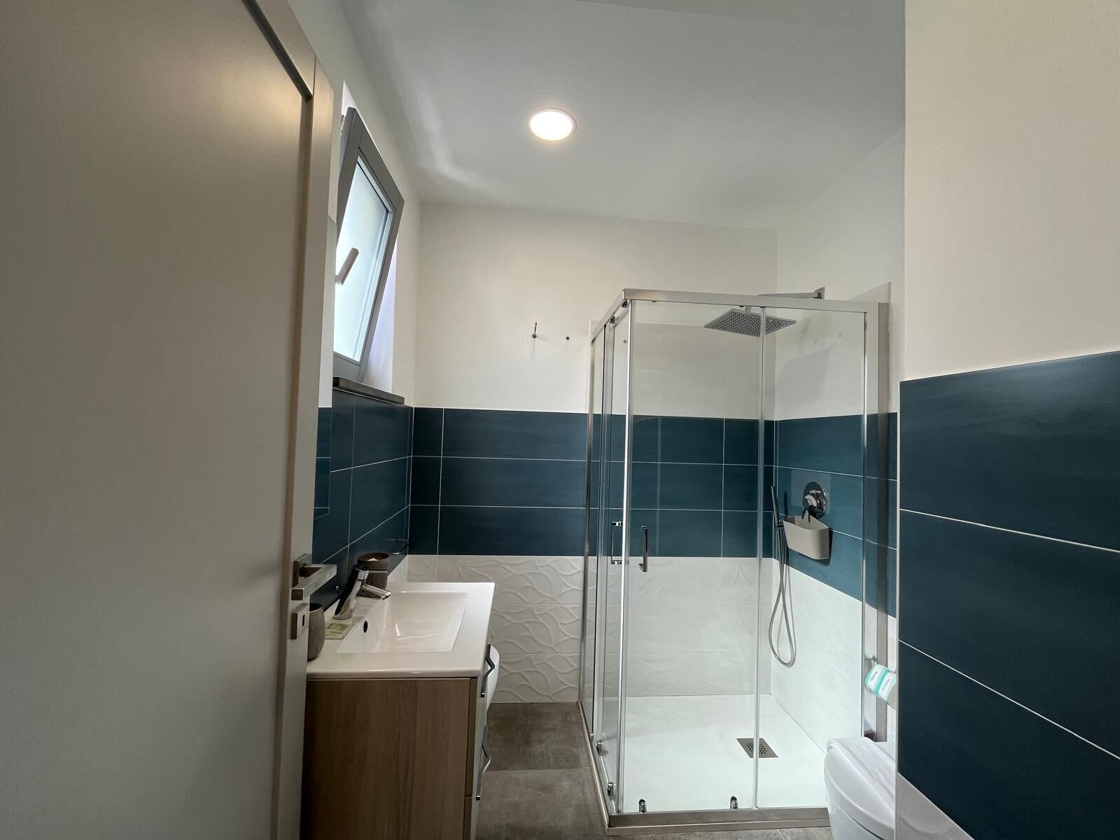 Un bagno moderno con cabina doccia in vetro, lavandino bianco e piastrelle blu scuro.