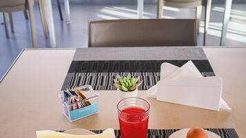 A breakfast setting with a plate of toast, a glass of red juice, a slice of melon, and a small dish of jam.
