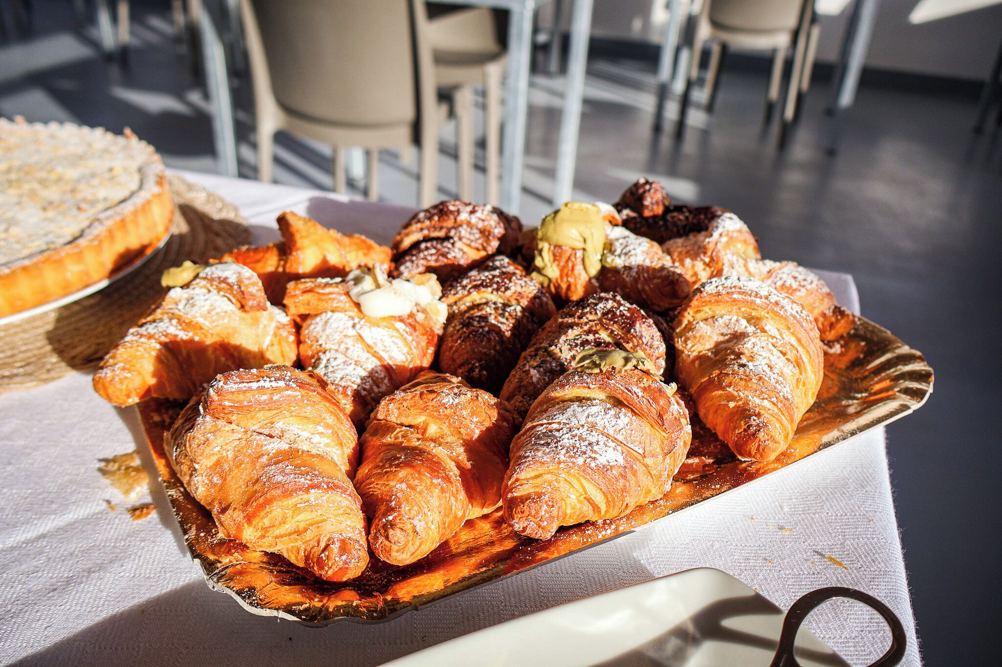 Un plateau rempli d’une variété de viennoiseries, notamment des croissants et d’autres produits de boulangerie, est posé sur une table.