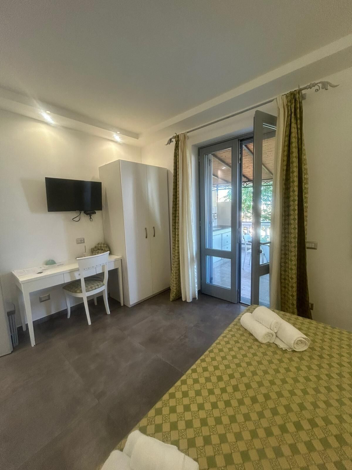 A hotel room with a bed, a desk, a chair, a television, and a sliding glass door leading to an outdoor area.