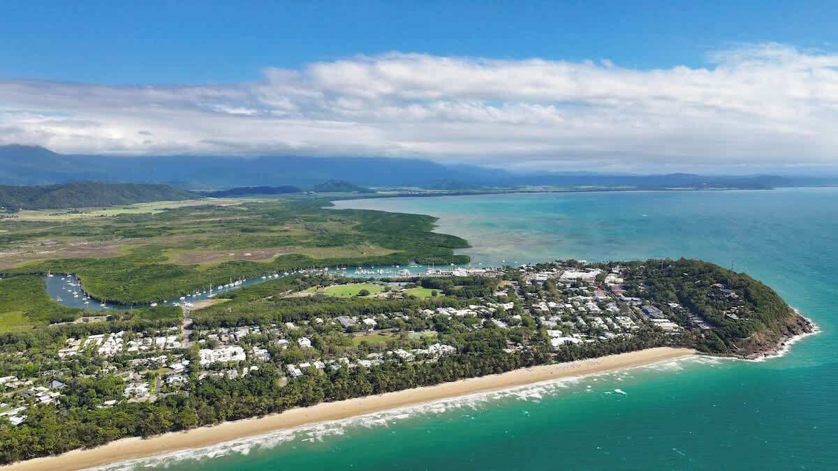 An aerial view of a coastal area with a beach, a small settlement, and a large body of water.