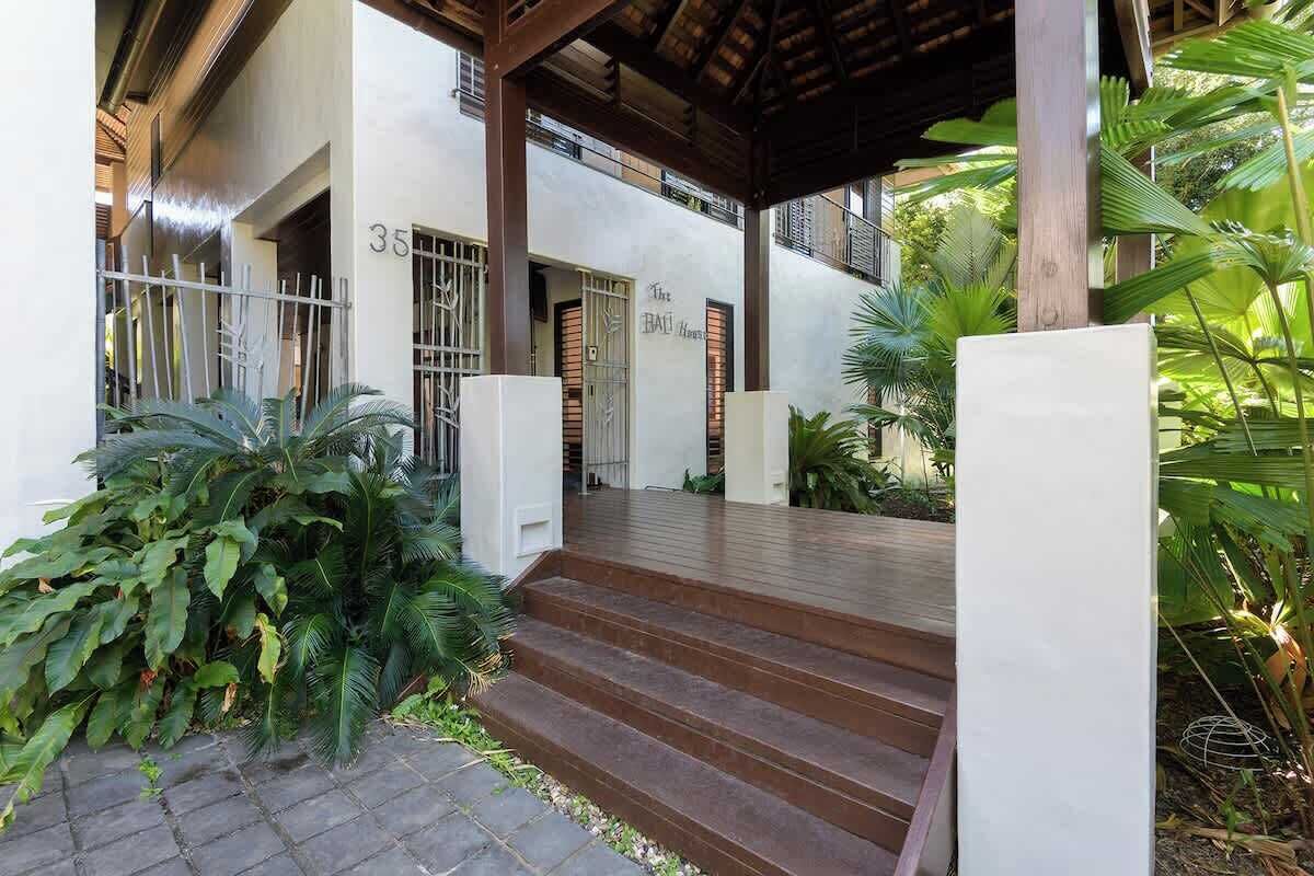 A building with a number '35' on the wall, a covered entrance with steps, and a garden area with tropical plants.