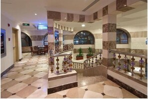 A hotel lobby with a check-in counter, a staircase with decorative railings, and a view of the city through large windows.