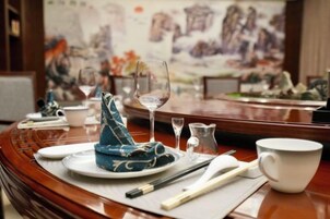 A traditional dining table with chopsticks, a teapot, and a cup, set against a backdrop of a painting.