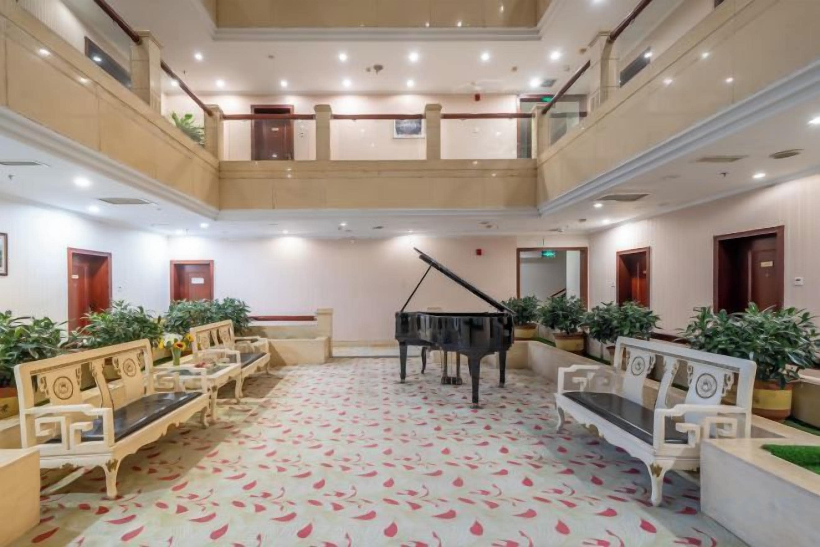 Un vestíbulo de hotel de varios niveles con un piano de cola, zonas de estar y plantas en macetas.