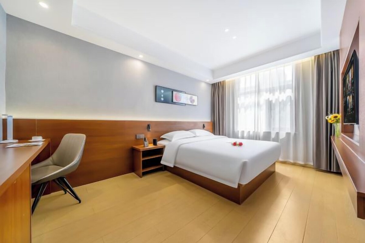 Una habitación de hotel con cama, escritorio, silla, mesita de noche y ventana con cortinas.