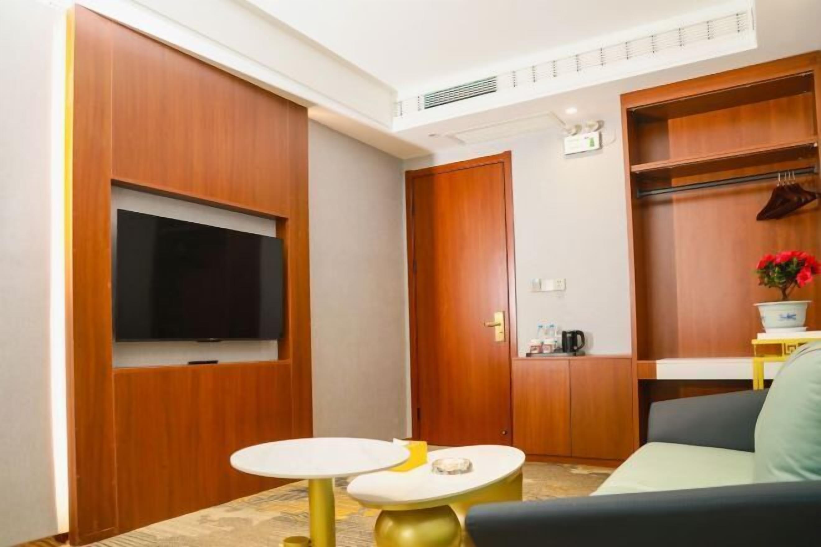 A compact living space with a TV mounted on a wall, a small round table, a sofa, and a wooden wardrobe.