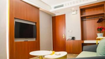 A compact living space with a TV mounted on a wall, a small round table, a sofa, and a wooden wardrobe.