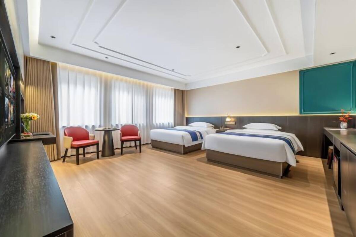 A hotel room with two beds, a desk, a chair, and a TV.