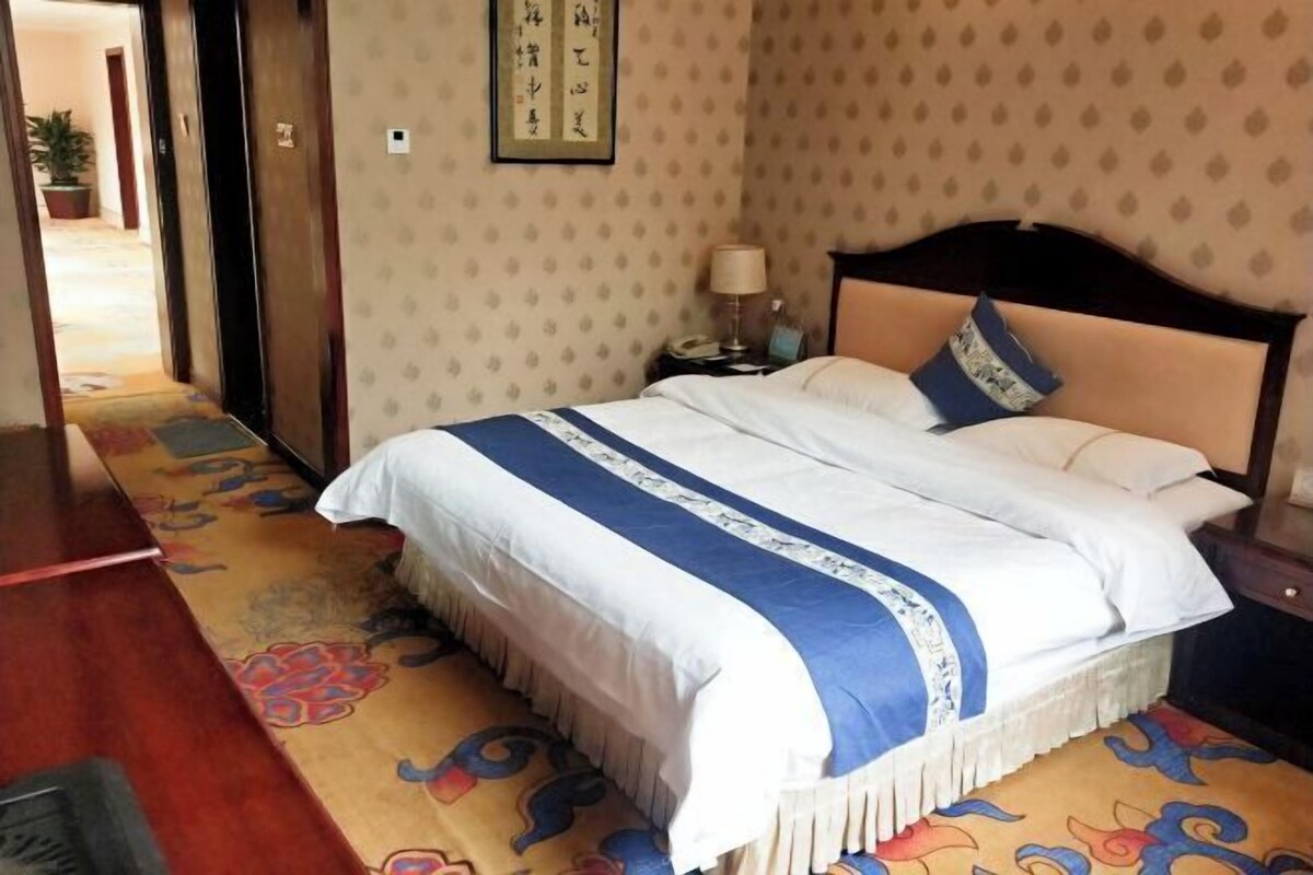 A hotel room with a bed, a nightstand, a lamp, and a wall with a framed picture.