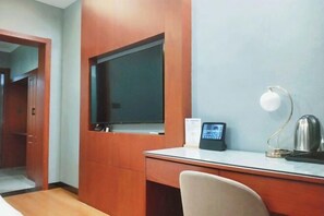 Una habitación de hotel con un escritorio de madera, una silla, un televisor, una lámpara de escritorio y una cafetera.