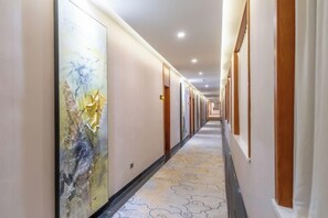 En hotellkorridor med dörrar på båda sidor, ett mönstrat golv och en stor, abstrakt målning på väggen till vänster.