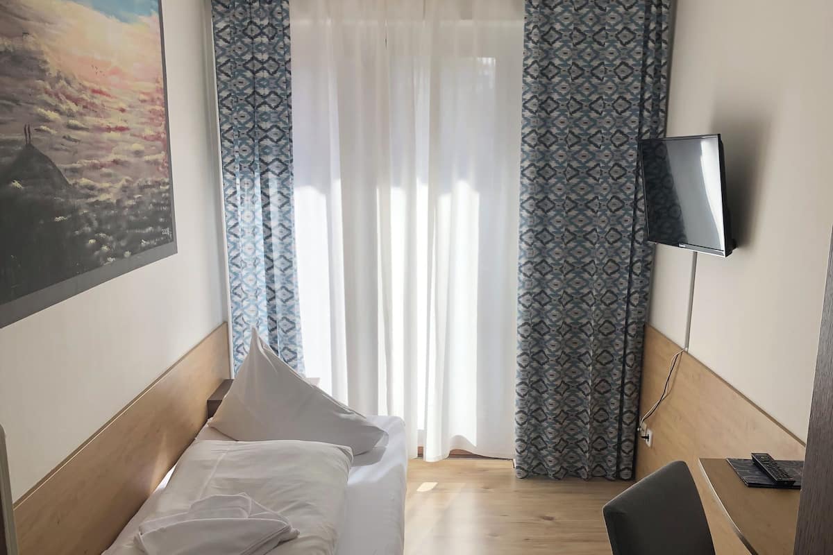 A hotel room with a bed, a desk, a chair, a TV, and a painting on the wall.