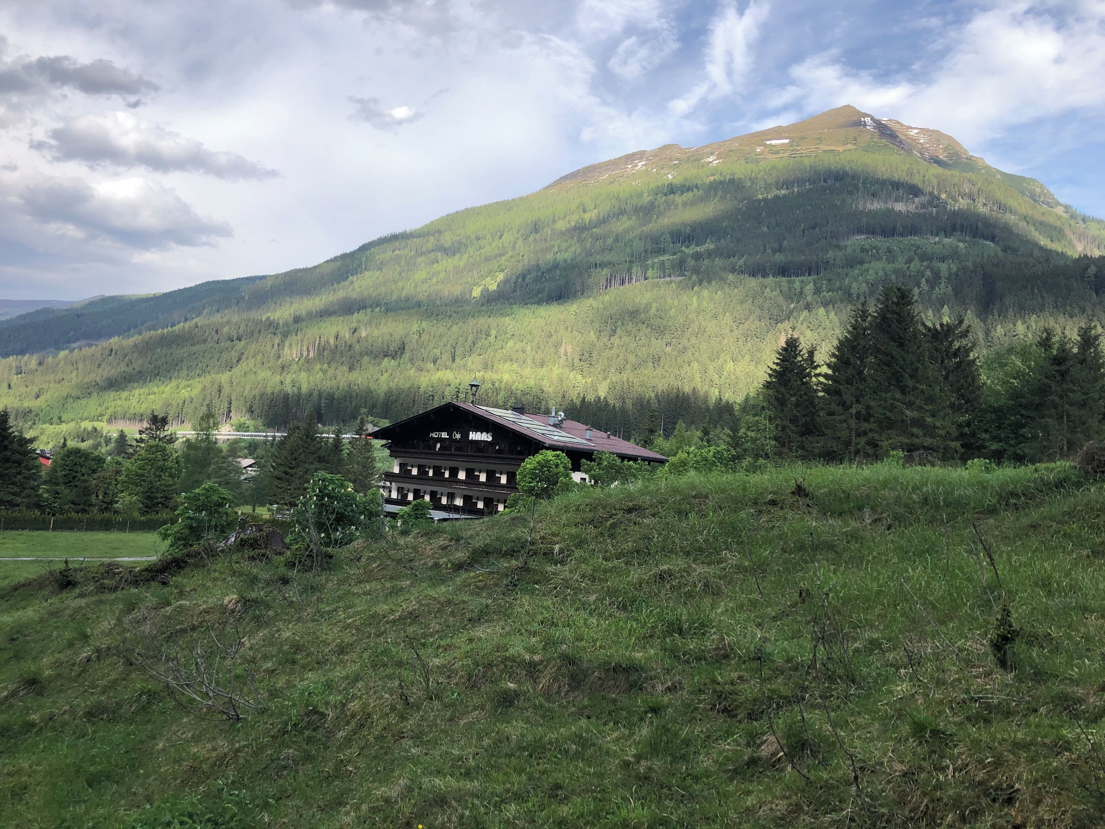Un chalet de montagne à l’architecture traditionnelle en bois, entouré d’une végétation luxuriante et adossé à une montagne boisée.