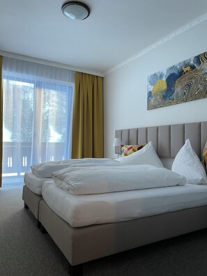 A hotel room with a large bed, a view of trees through sheer curtains, and a painting on the wall. - Hotel HAAS (Bad Gastein)
