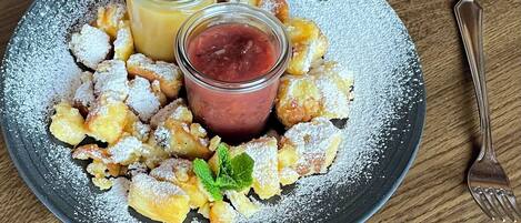 A plate of fritters with powdered sugar, two small glasses of fruit compote, and a mint garnish.