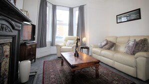 A living room with a beige sofa, a wooden coffee table, a fireplace, and a television. - Sleeps 9 - Large Period Property -beautiful Refurb (Newcastle-upon-Tyne)