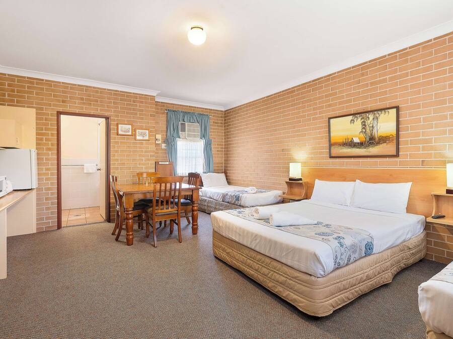 Habitación de hotel con dos camas, una mesa de comedor con sillas, un refrigerador y un cuadro en la pared.