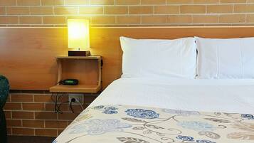 Habitación de hotel con pared de ladrillo, cama con ropa blanca, mesita de noche con lámpara y un cuadro sobre la cama.