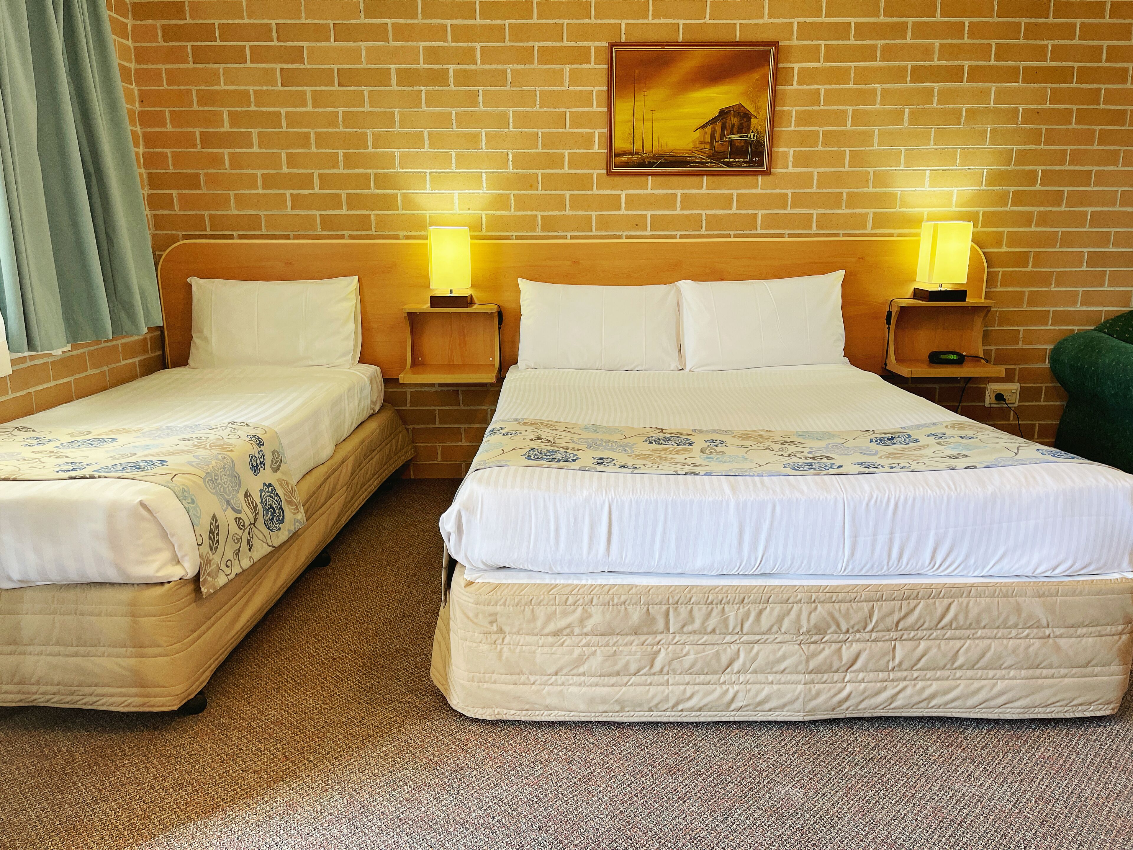 A hotel room with two single beds, a large bed, a brick wall, a painting, and two bedside lamps.