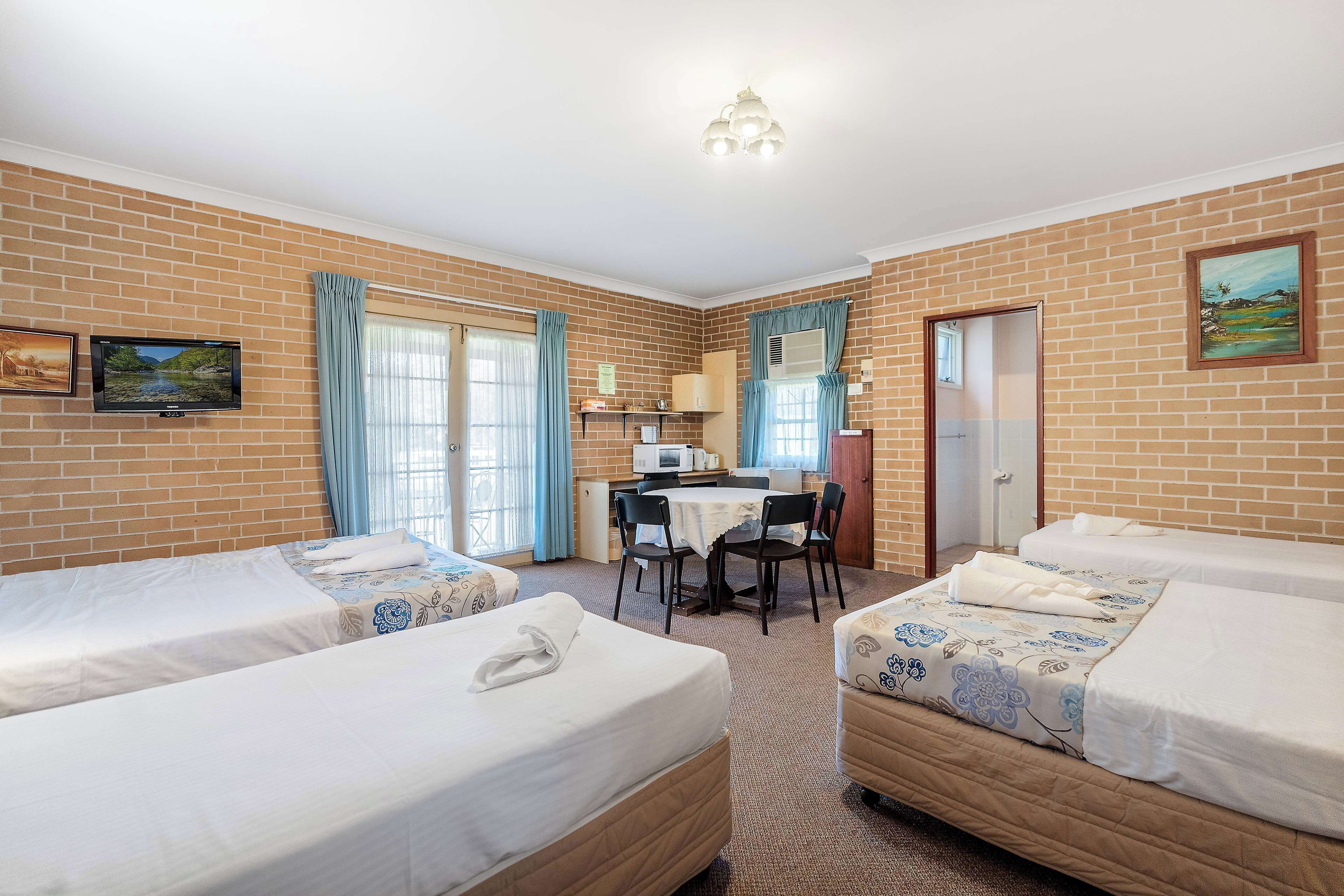 A hotel room with two single beds, a desk with a chair, a small kitchenette, and a bathroom door.