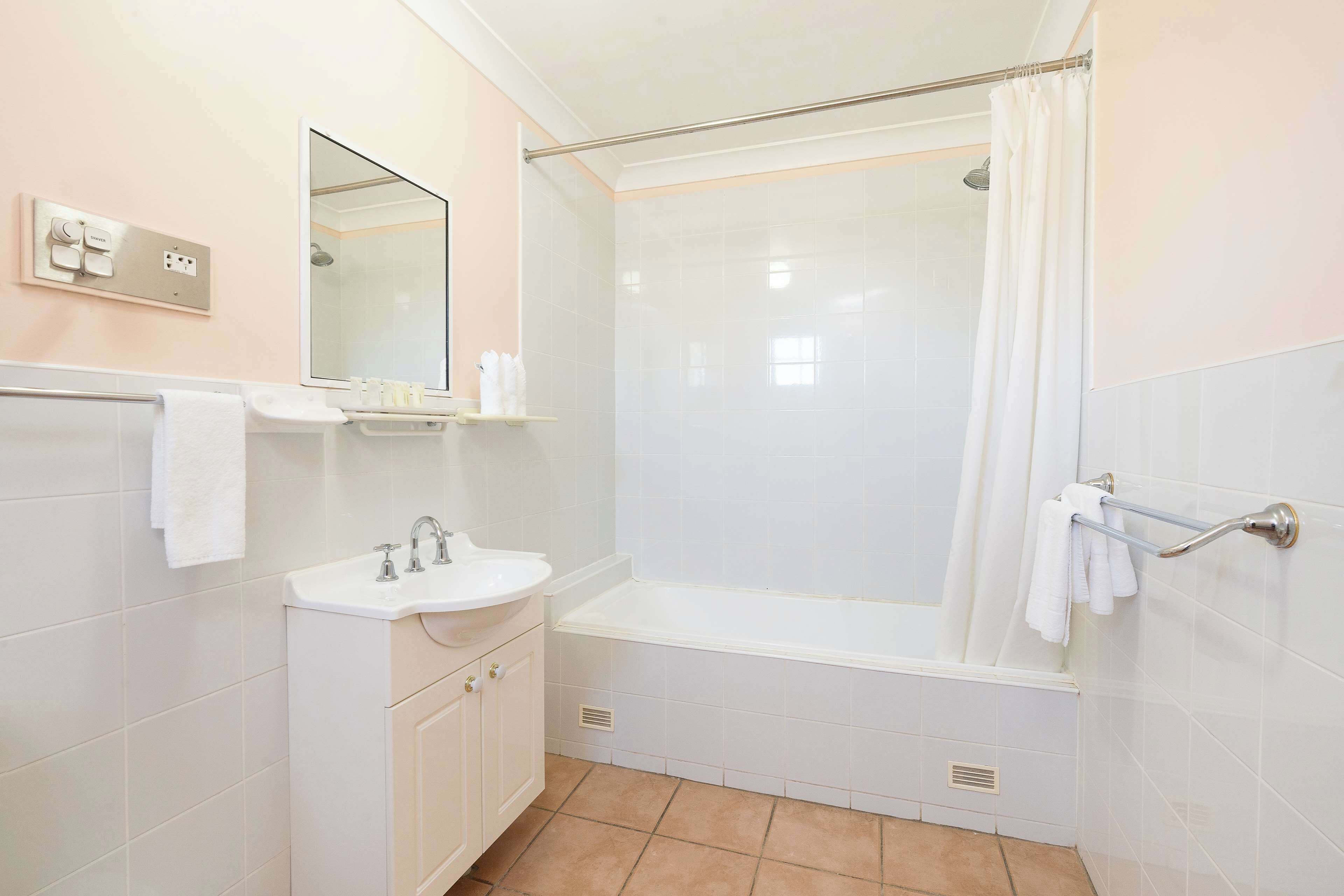 Un baño con lavamanos, espejo, ducha y toallero.