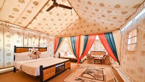A bedroom with a bed, a chair, a table, and a ceiling fan. - Sam Resort and Camp (Jaisalmer)