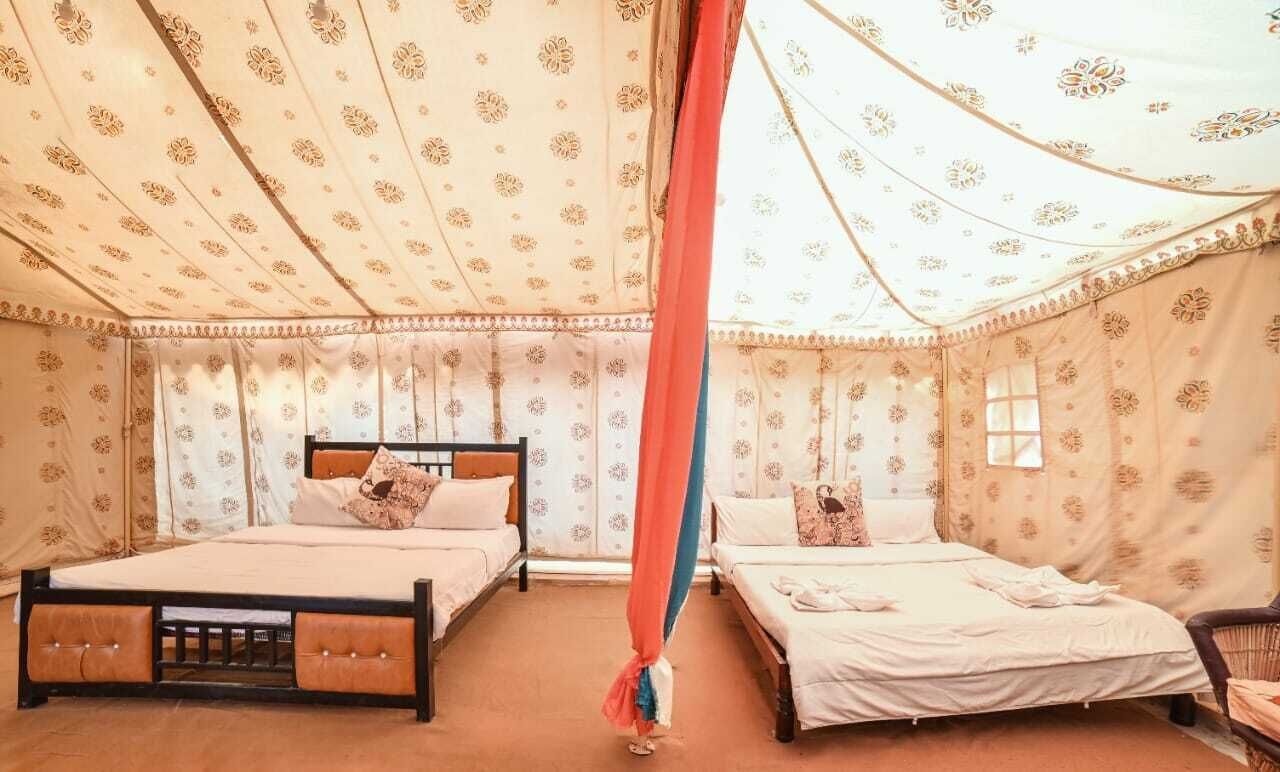 A room with two beds, a canopy, patterned walls, and a window.
