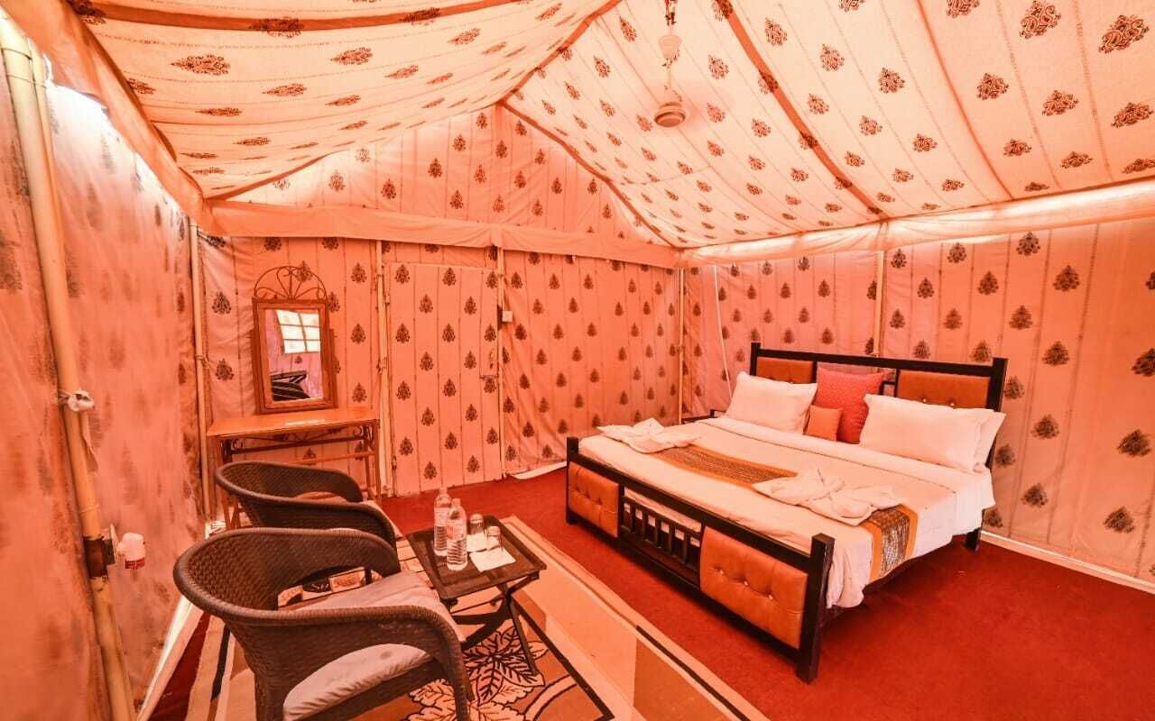 A tented room with a bed, two chairs, a small table, and a mirror.