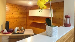 A wooden interior with a white cabinet, a table with tea sets, and a potted orchid. - Whispering Pines Haven (Redmond)