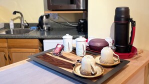 A kitchen area with wooden cabinets, a microwave, a coffee maker, and a tray with teacups and a teapot. - Whispering Pines Haven (Redmond)