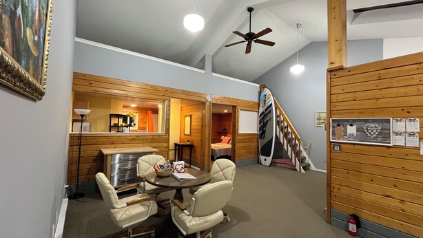 A room with a dining table and chairs, a ceiling fan, a wooden staircase, and a surfboard leaning against the wall. - Whispering Pines Haven (Redmond)
