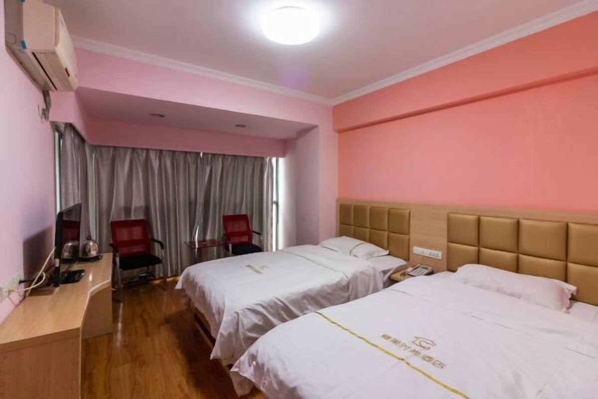 Habitación de hotel con dos camas, un escritorio, una silla y un ventanal con cortinas.