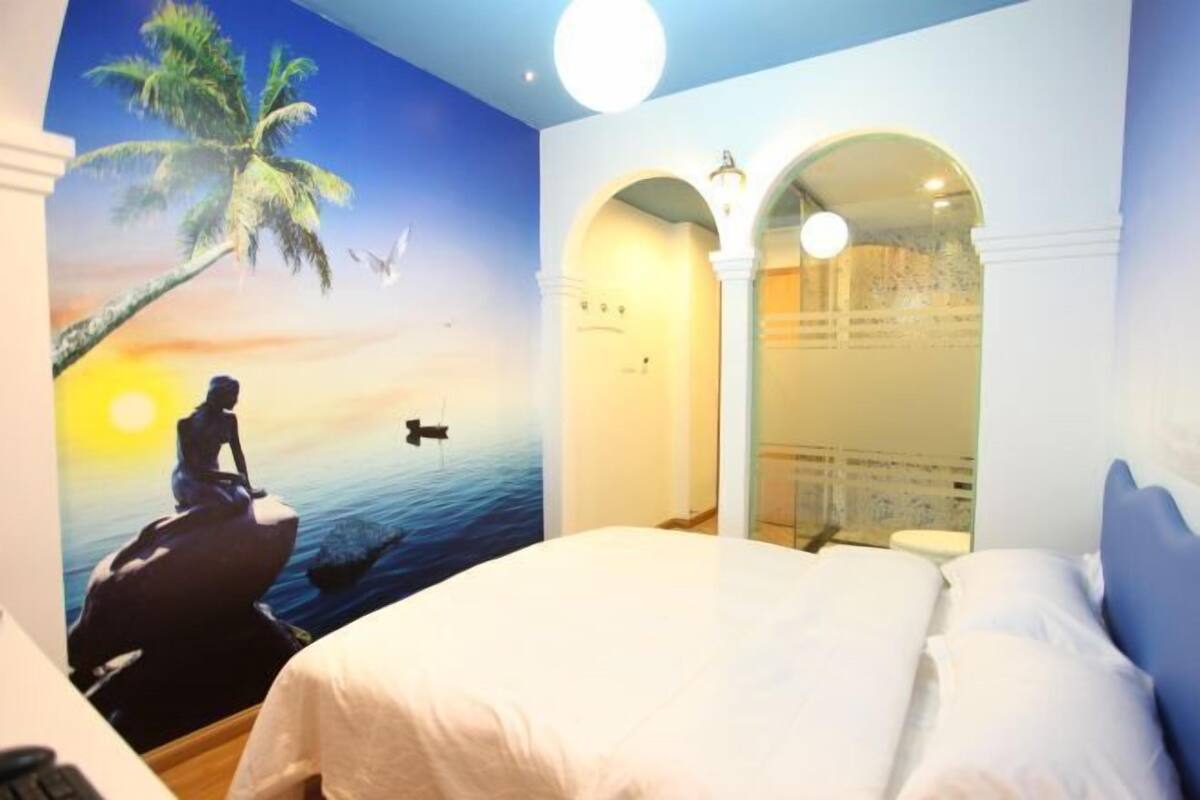 Un dormitorio con cama, un mural de un atardecer con palmeras y vistas a través de un arco.