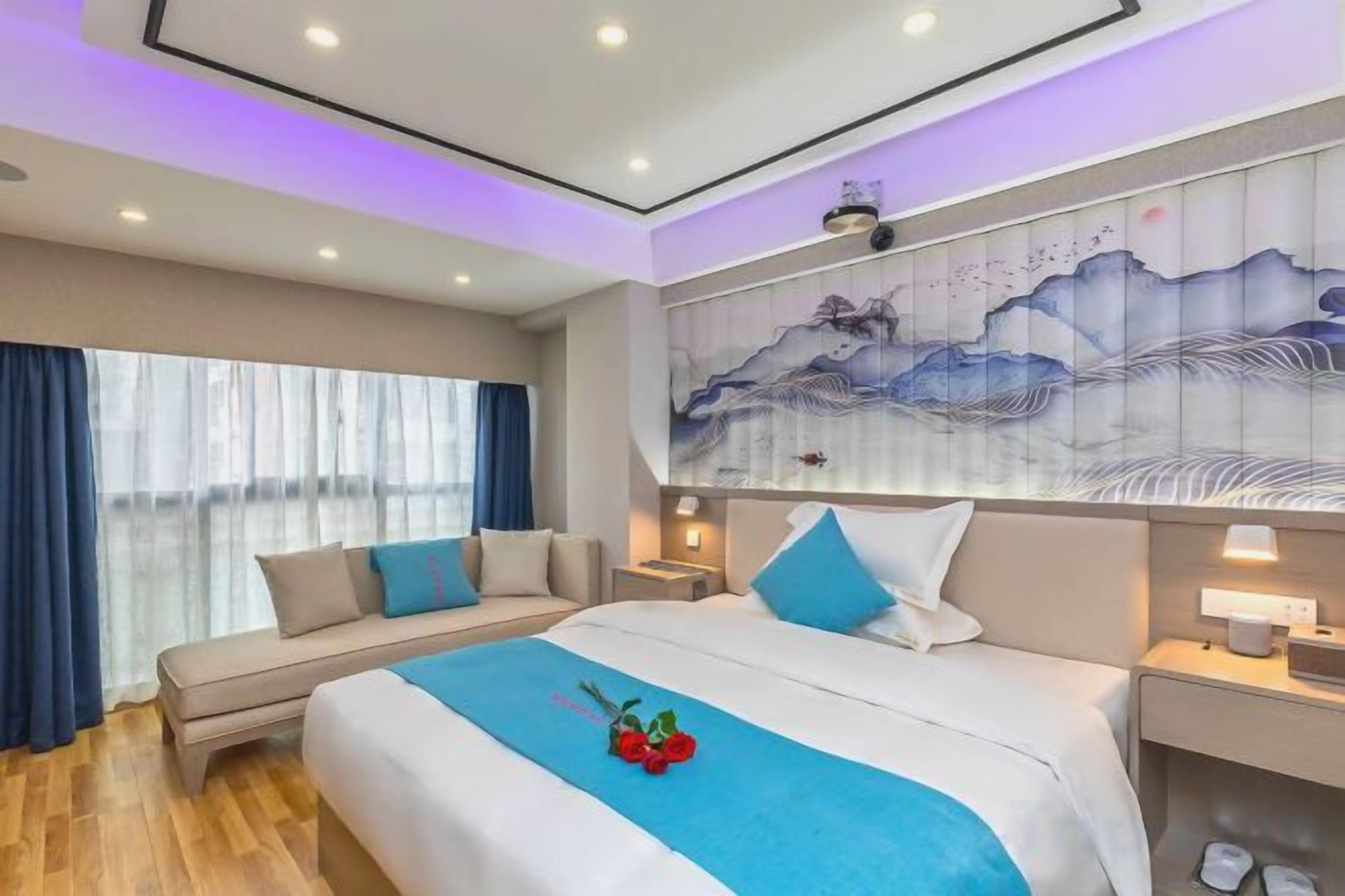 A hotel room with a bed, a sofa, a nightstand, and a wall painting.