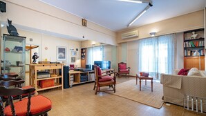 A spacious living room with a wooden floor, a sofa, a desk with a computer, and a bookshelf. - Syntagma square 1 bedrm 4 persons apartment by MPS (Athina)