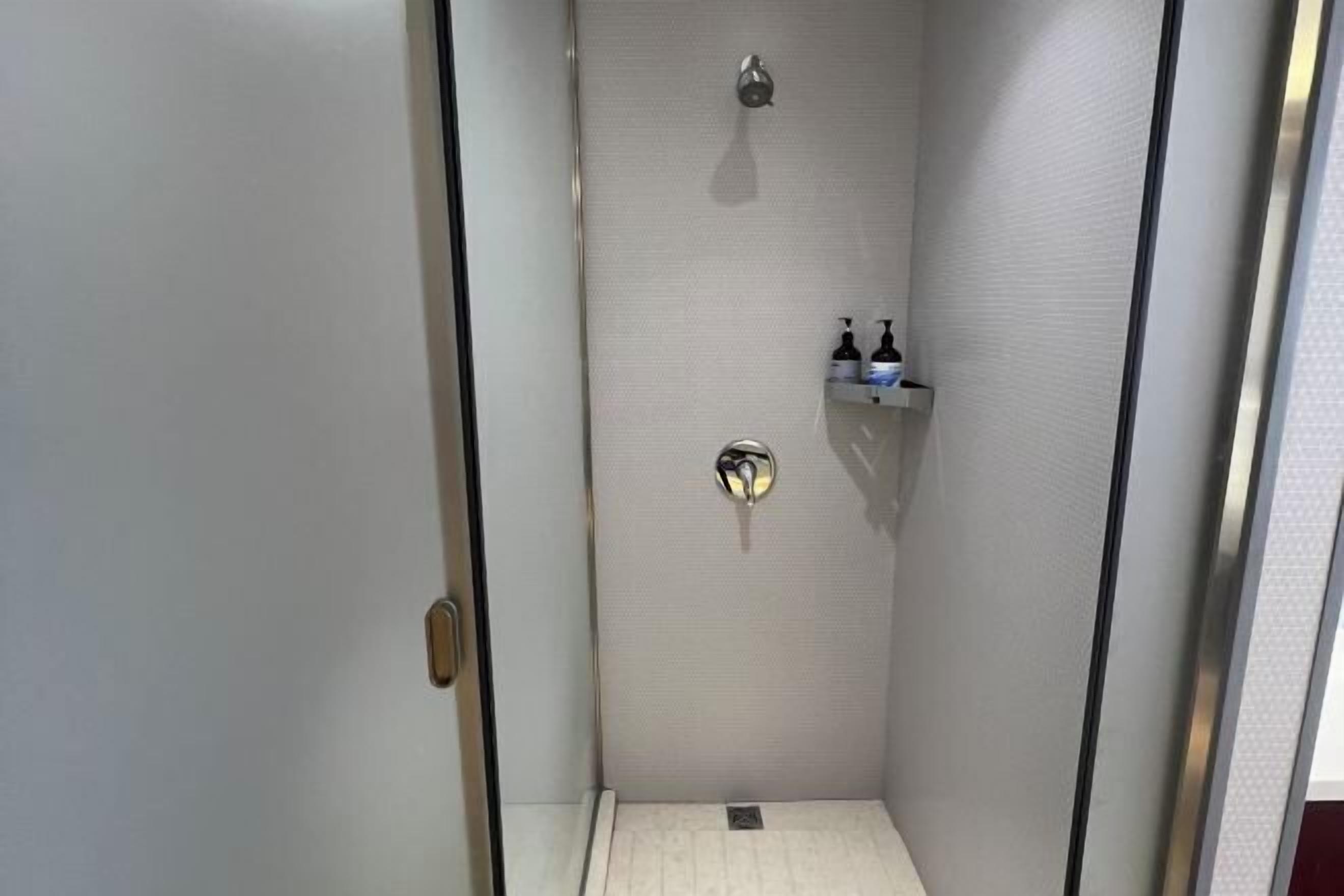 Piccola cabina doccia con porta in vetro, soffione e ripiano con articoli da toilette.