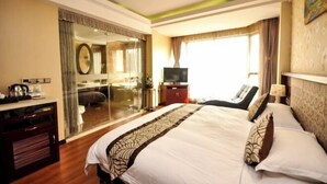 A hotel room with a large bed, a TV, a desk with a coffee maker, and a sliding glass door leading to a bathroom. - Xi Xi Holiday Hotel (Zhoushan)