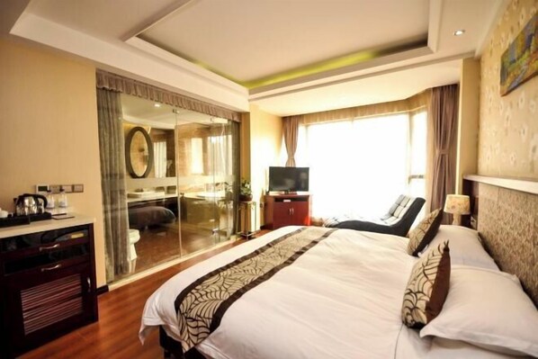 A hotel room with a large bed, a TV, a desk with a coffee maker, and a sliding glass door leading to a bathroom. - Xi Xi Holiday Hotel (Zhoushan)