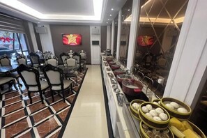 Zona pranzo con un lungo tavolo, sedie, buffet con contenitori per il cibo e televisione a parete.